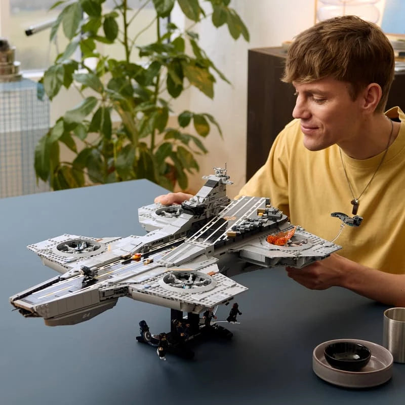 Man holding the completed LEGO Marvel S.H.I.E.L.D. Helicarrier above its black display stand and minifigures