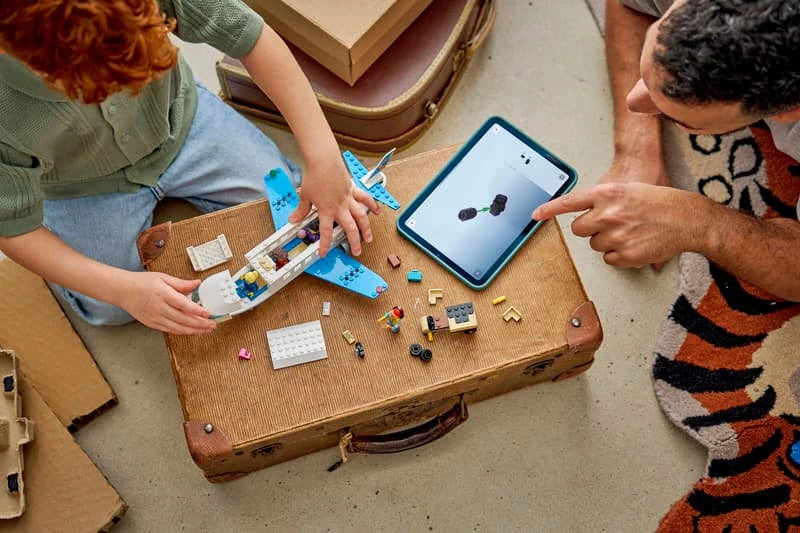 Child and adult building LEGO Passenger Jet on a table with a tablet nearby