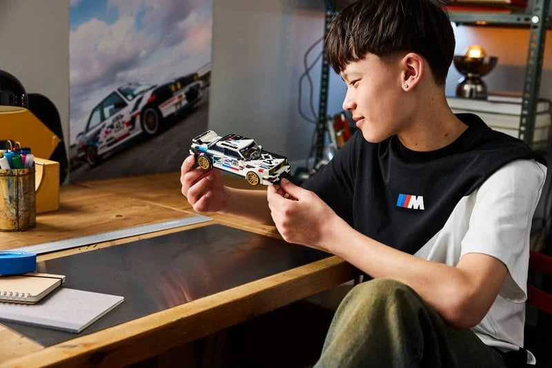 Builder holding the LEGO Speed Champions BMW M3 (E30) 77263 model at a desk