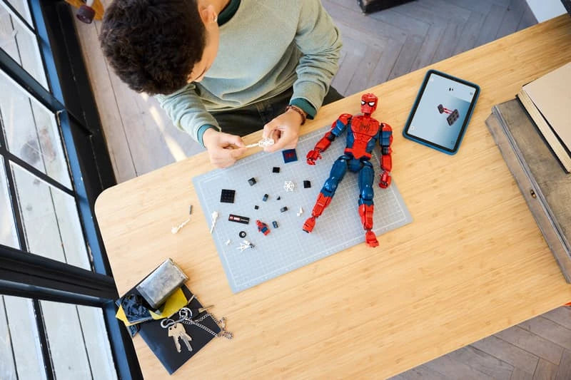 Child building a LEGO Spider-Man figure at a table with tablet instructions