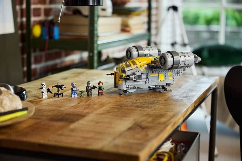 Completed LEGO Star Wars The Razor Crest displayed on a wooden table with Grogu and four minifigures arranged beside the ship