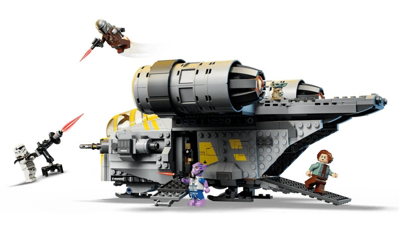 Side view of the LEGO Razor Crest with its ramp lowered, Grogu on top, The Mandalorian flying above and minifigures positioned around the ship