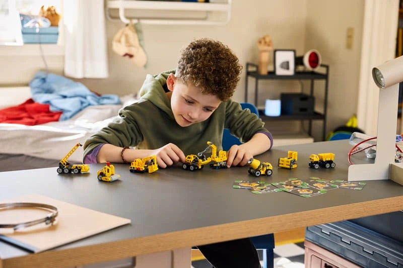 Child arranging a lineup of LEGO Technic Mighty Machines 42233 construction vehicles on a table
