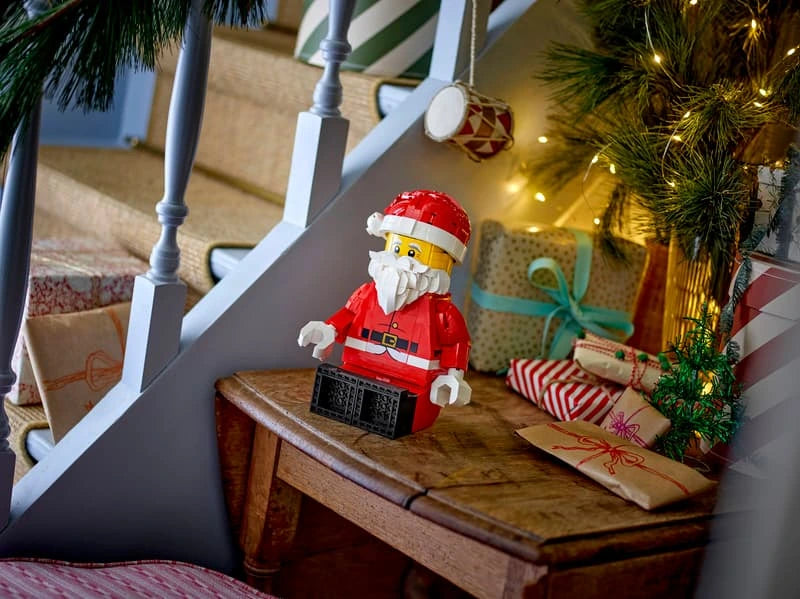 LEGO Santa figure seated on a wooden table beside wrapped presents and a Christmas tree