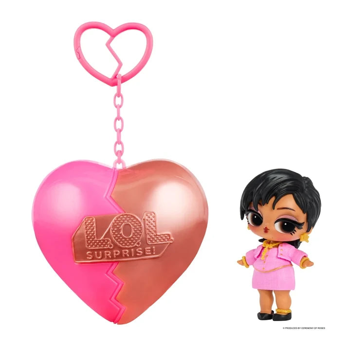 L.O.L. Surprise Music Festival Headliners Tots doll with short black hair, a pink jacket and skirt, gold jewellery and black shoes, displayed beside a pink and rose gold heart shaped capsule with a matching keychain.