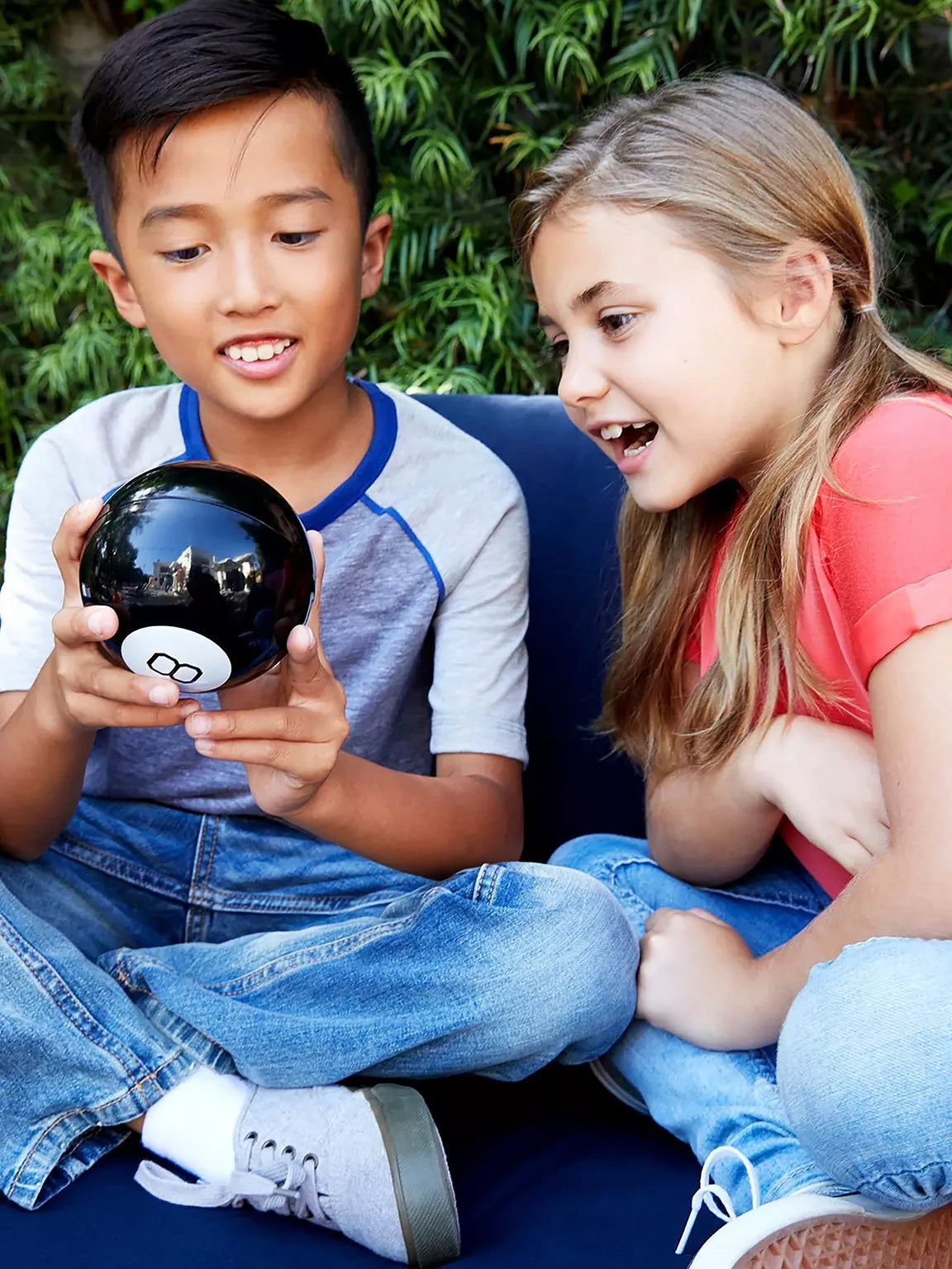 Two children looking at a black Magic 8 Ball held in front of them
