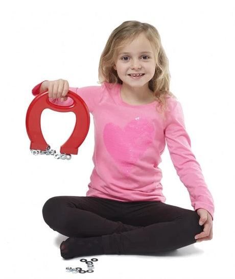Child sitting at table exploring metal objects using red Massive Magnet toy during a science activity