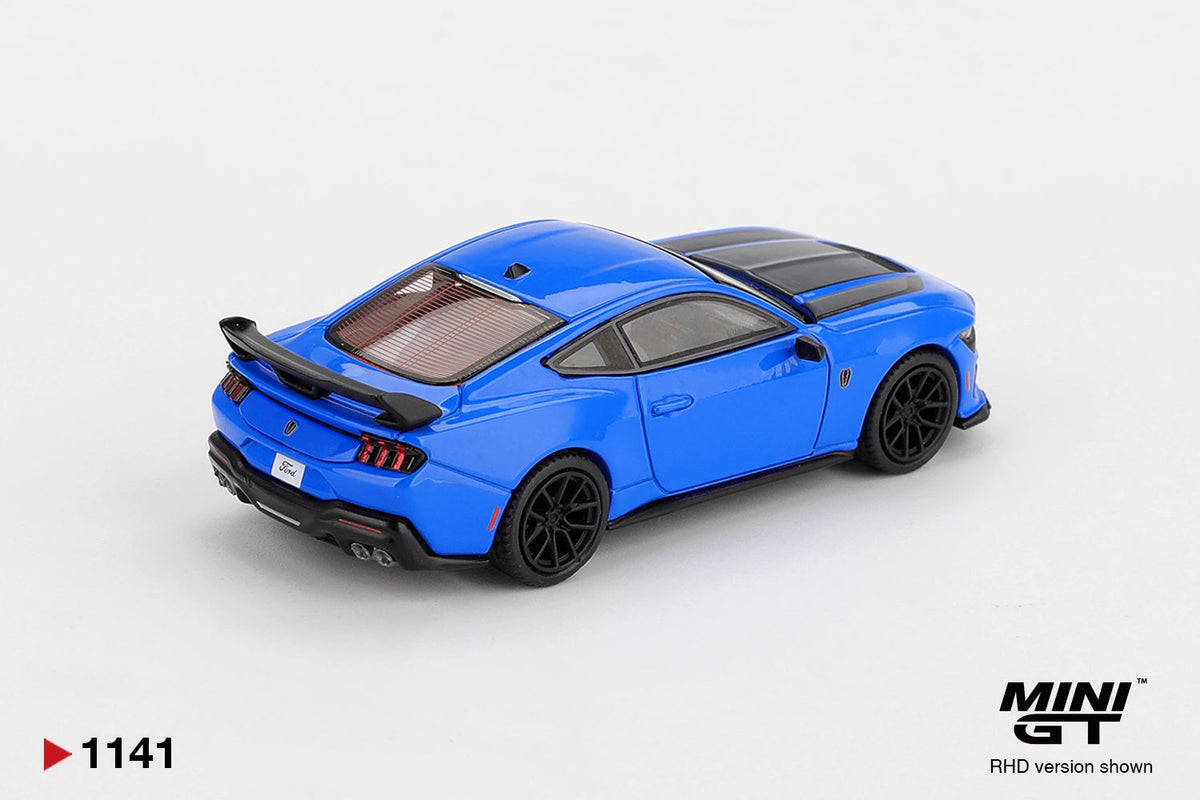 Rear three quarter view of Mini GT Ford Mustang Dark Horse 2024 Grabber Blue RHD showing the large black rear spoiler, triple vertical taillights, quad exhaust outlets and black wheels.