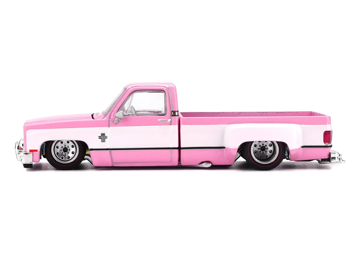 Side profile of Mini GT Chevrolet Silverado Dually Vintage Spec V2 showing pink and white bodywork, lowered stance, silver wheels and extended rear wheel arches