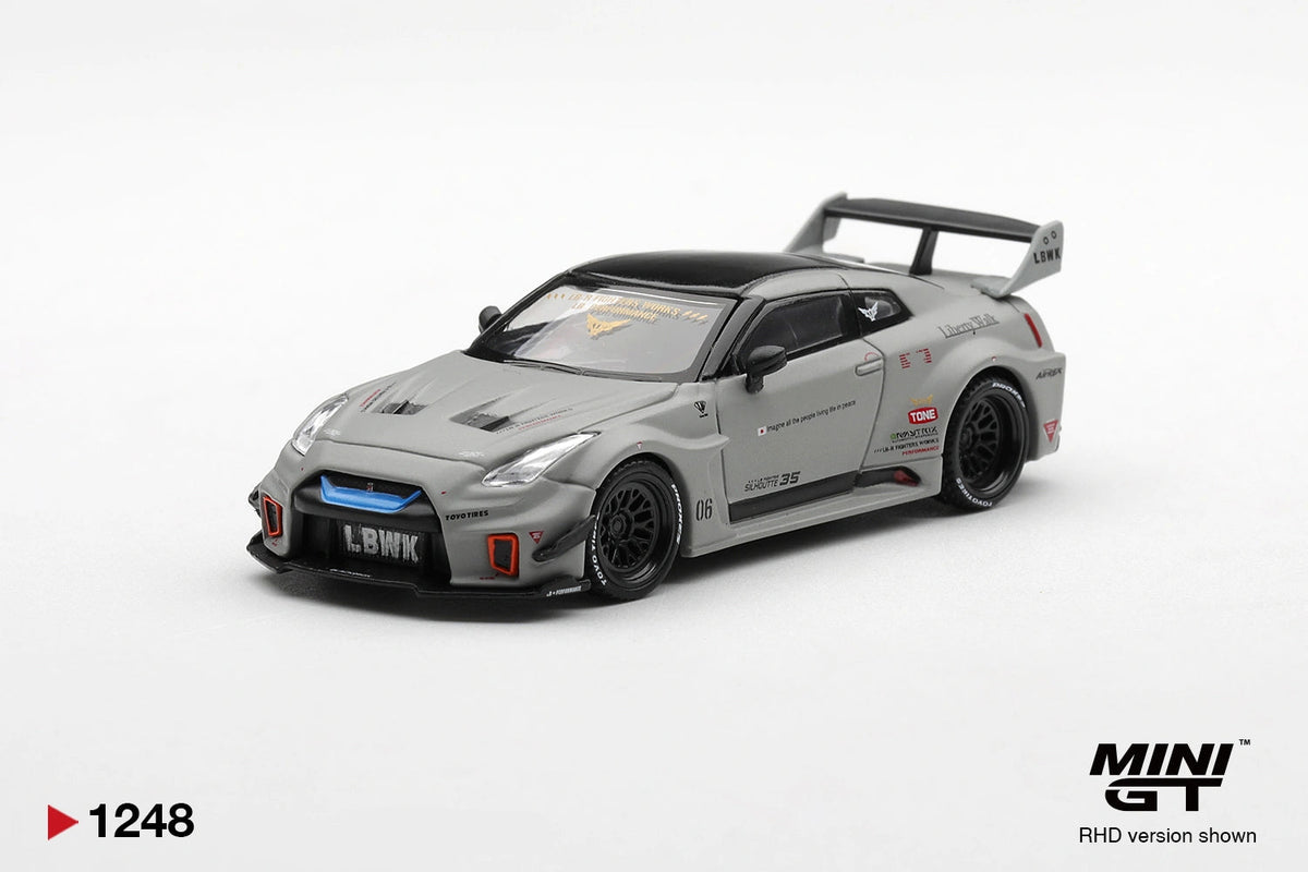 Front three-quarter view of Mini GT Nissan LB-Silhouette WORKS GT 35GT-RR Matt Grey RHD showing the blue grille accent, black bonnet vents, extended front splitter, Liberty Walk graphics and black racing wheels.