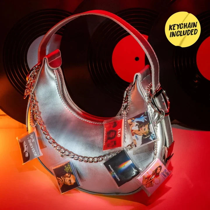 Silver handbag decorated with miniature album cover keychains featuring artists including TLC, Britney Spears and Imagine Dragons, against a background of black vinyl records.