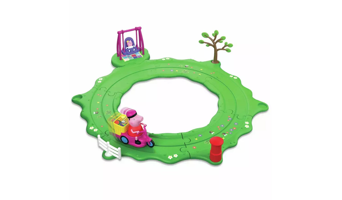 Peppa & Evie Fun in the Park Playset assembled on a white background, with a circular green road track, Peppa riding a pink bike with a yellow basket, Evie in a purple swing, a tree, white fence and red post box.
