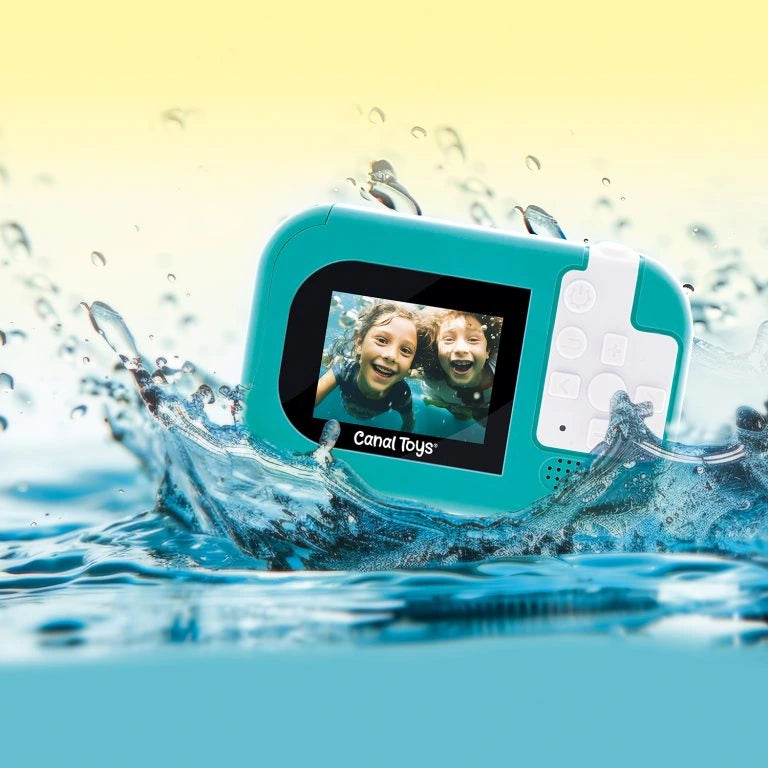 Rear view of the turquoise Photo Creator Waterproof Digital Camera surrounded by splashing water, showing its colour screen displaying two smiling children underwater and white camera control buttons.