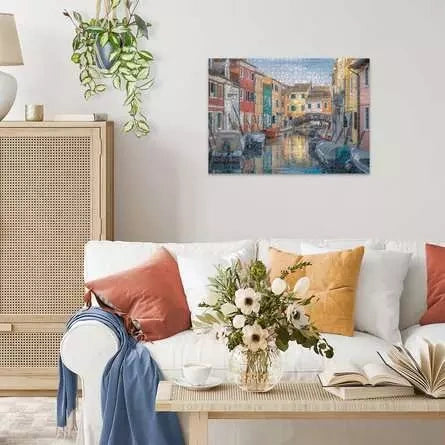 Completed Ravensburger Burano Italy puzzle displayed on a wall above a sofa, showing the colourful canal houses