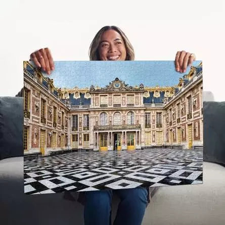 Woman holding the completed Ravensburger Château de Versailles puzzle showing the palace courtyard and black and white paving