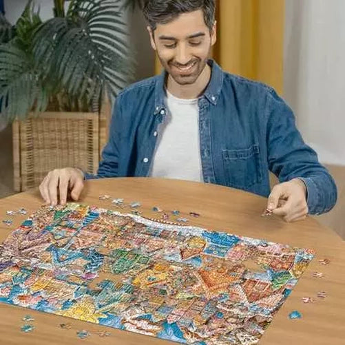 Man assembling the Ravensburger Christmas Cookie Village jigsaw puzzle on a table with loose pieces around the colourful village scene