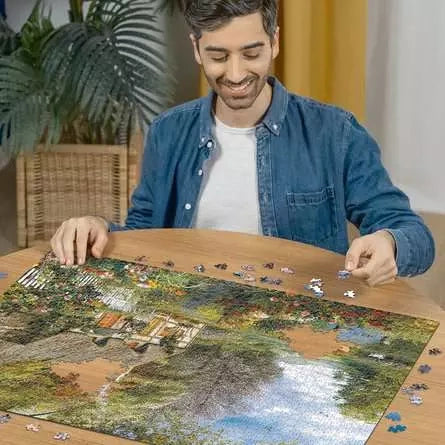 Man assembling the Ravensburger Country Cottage jigsaw puzzle on a table with loose pieces around the image