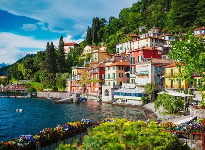 Ravensburger Lake Como Italy puzzle artwork showing colourful lakeside buildings, green hills, blue water and flowers along the shore