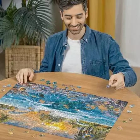Man assembling the Ravensburger Underwater Island jigsaw puzzle on a table with loose puzzle pieces around the image