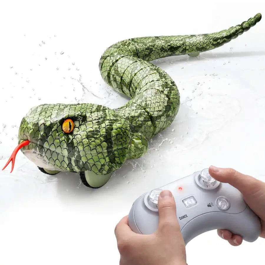Close-up of the green amphibious RC snake with its long curved body, reptile scale pattern, yellow eyes and red tongue. Two hands operate a grey remote controller in the foreground, with water splashes surrounding the snake.