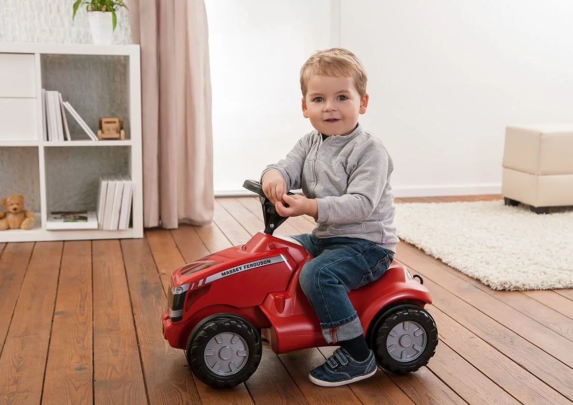Young child riding red Rolly Minitrac Massey Ferguson toy tractor indoors on wooden floor – Ireland