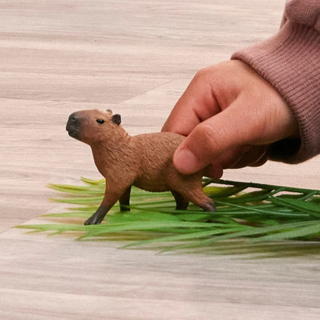 Schleich Capybara figure held above green leaves