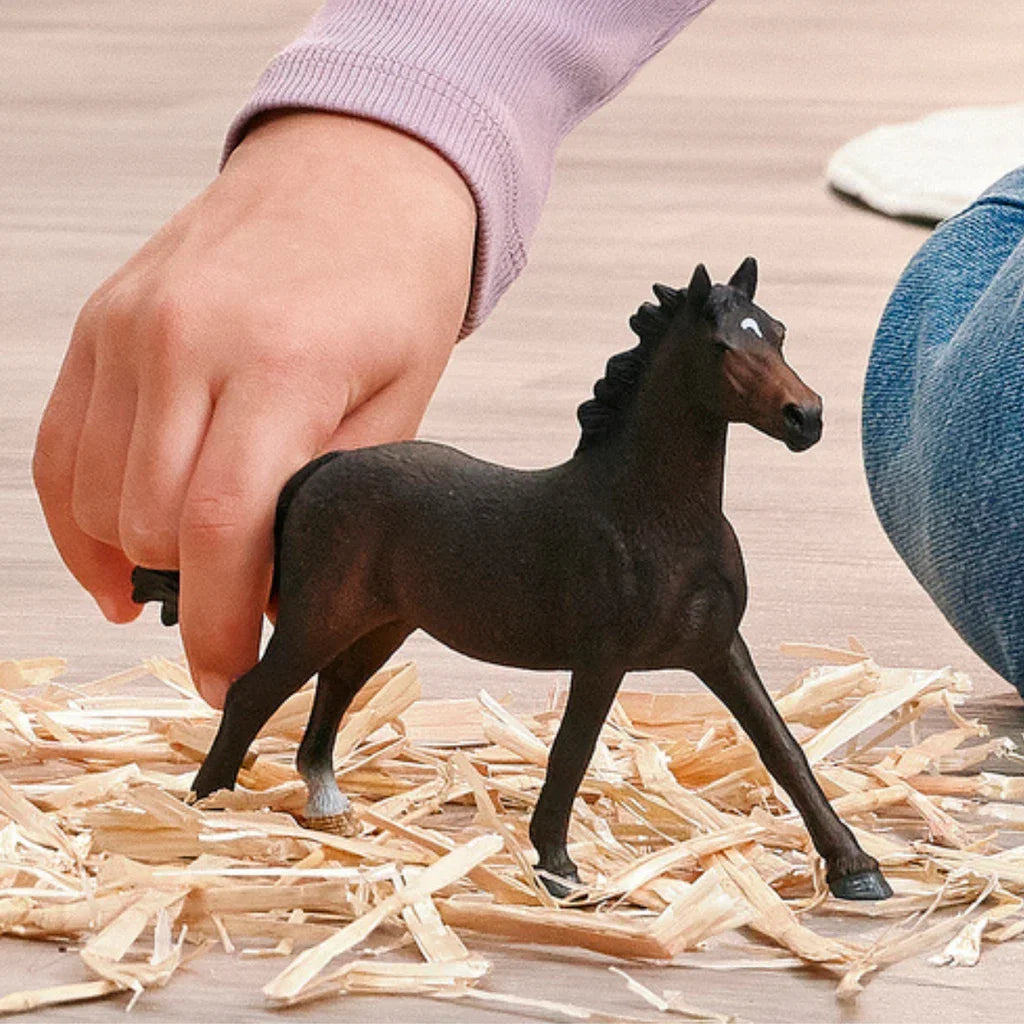 Schleich English Thoroughbred Mare figure standing on straw beside a child's hand