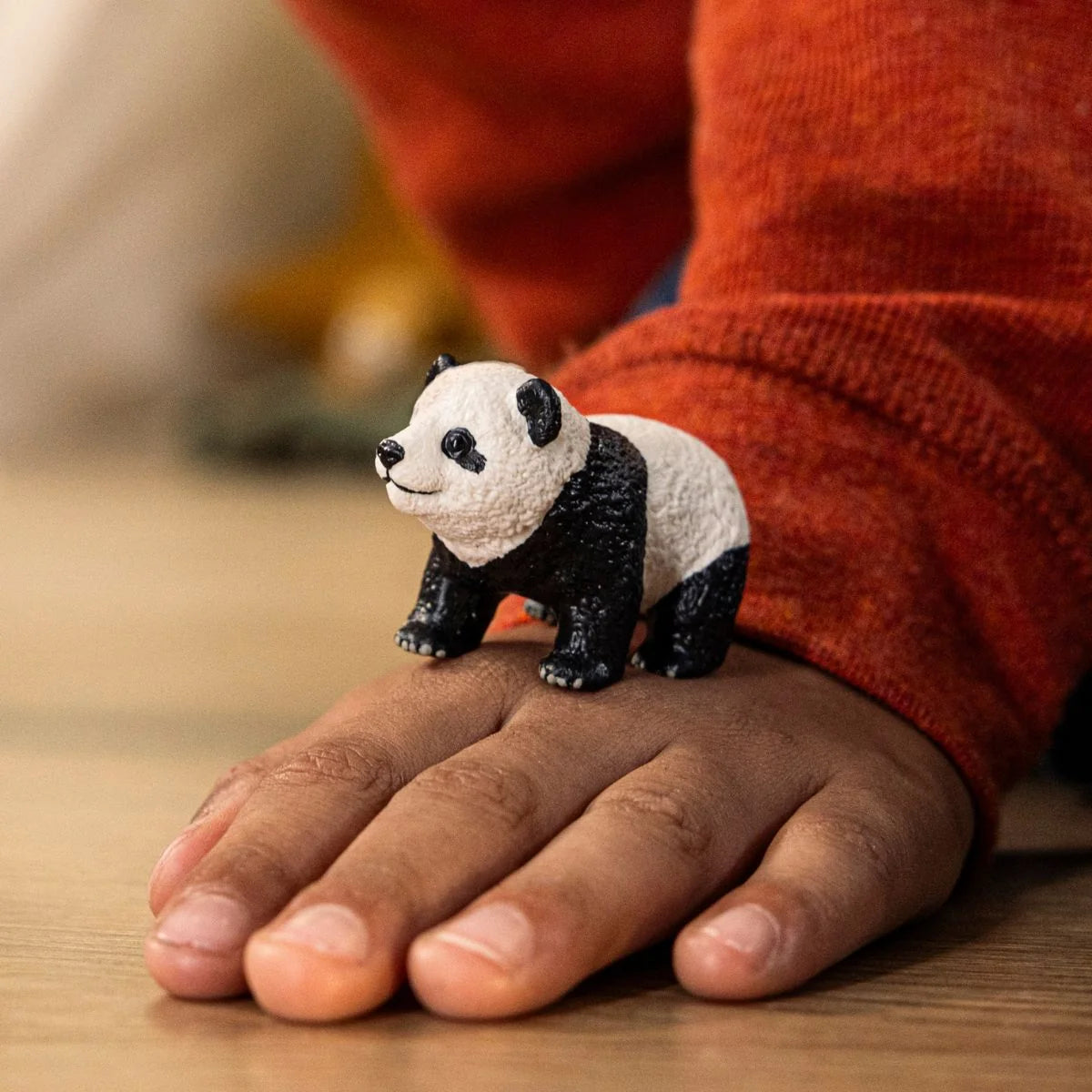 Schleich Giant Panda Cub figure standing on a hand with a red sleeve visible behind it.