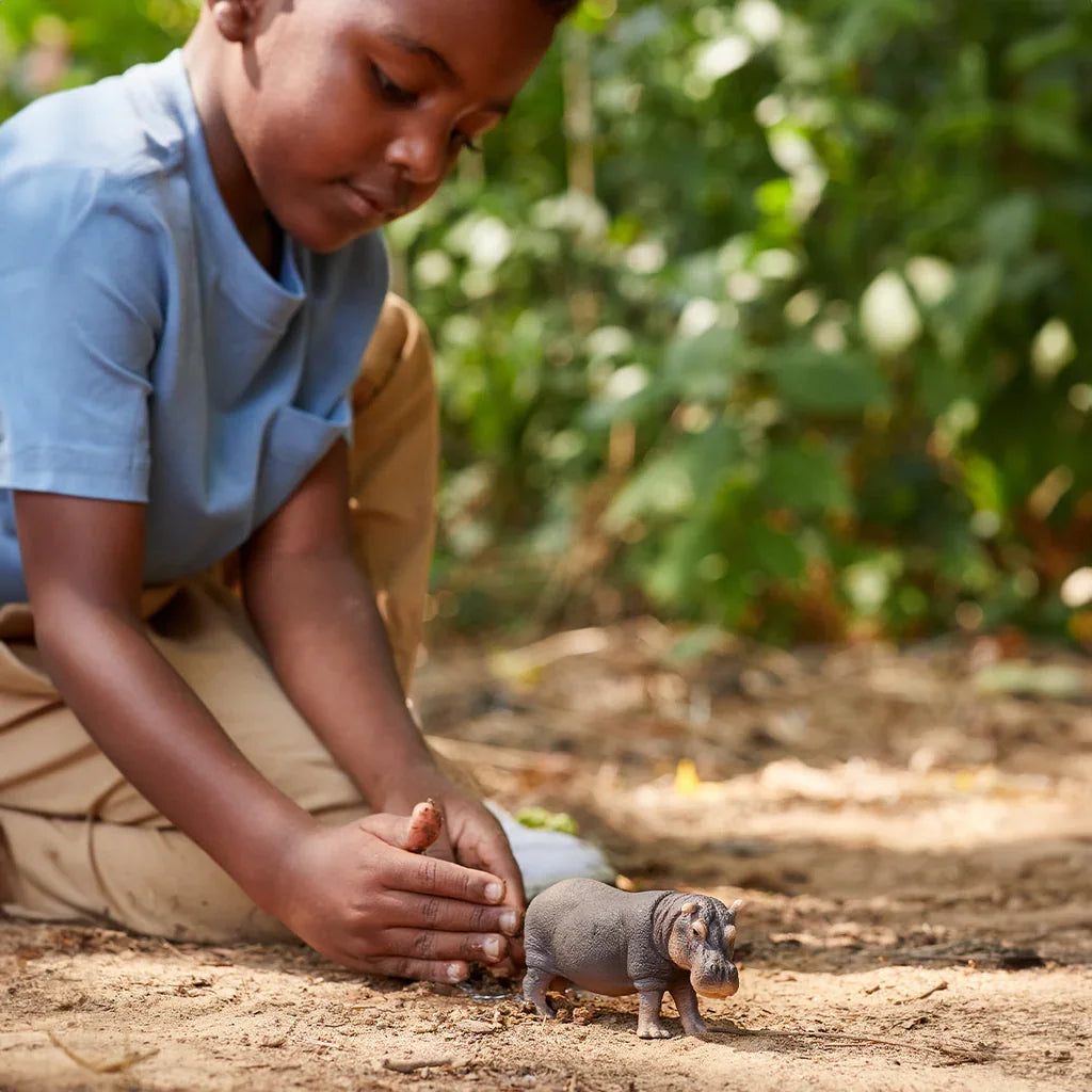 Schleich hippopotamus figure on soil with a child gathering soil behind it.