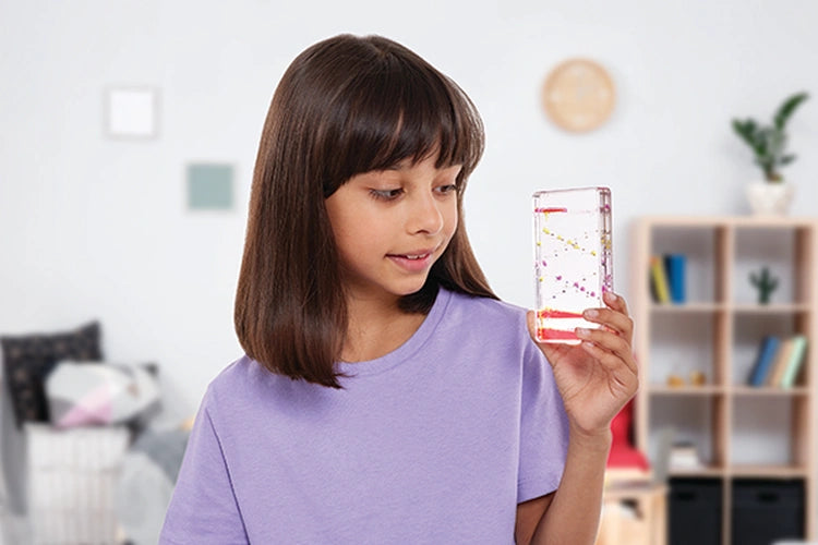 Girl holding a Sensory Motion Bubbler Stair upright and watching coloured liquid droplets move through the clear container