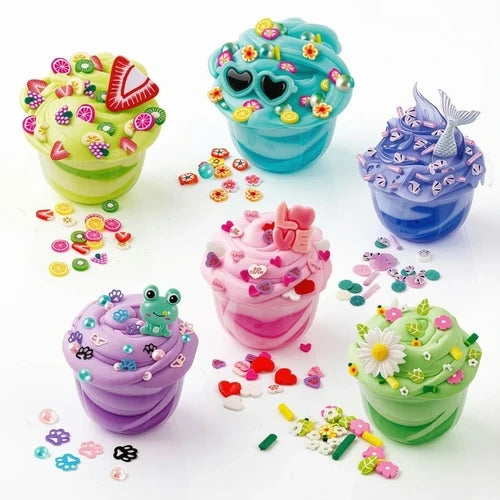 Six colourful So Slime creations in clear pots, decorated with miniature sweets, flowers, heart shaped sunglasses, a frog charm, pink hearts and a blue mermaid tail, with loose decorations scattered around them.