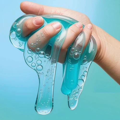 Close-up of a hand squeezing and stretching transparent turquoise slime containing numerous visible air bubbles against a pale blue background.