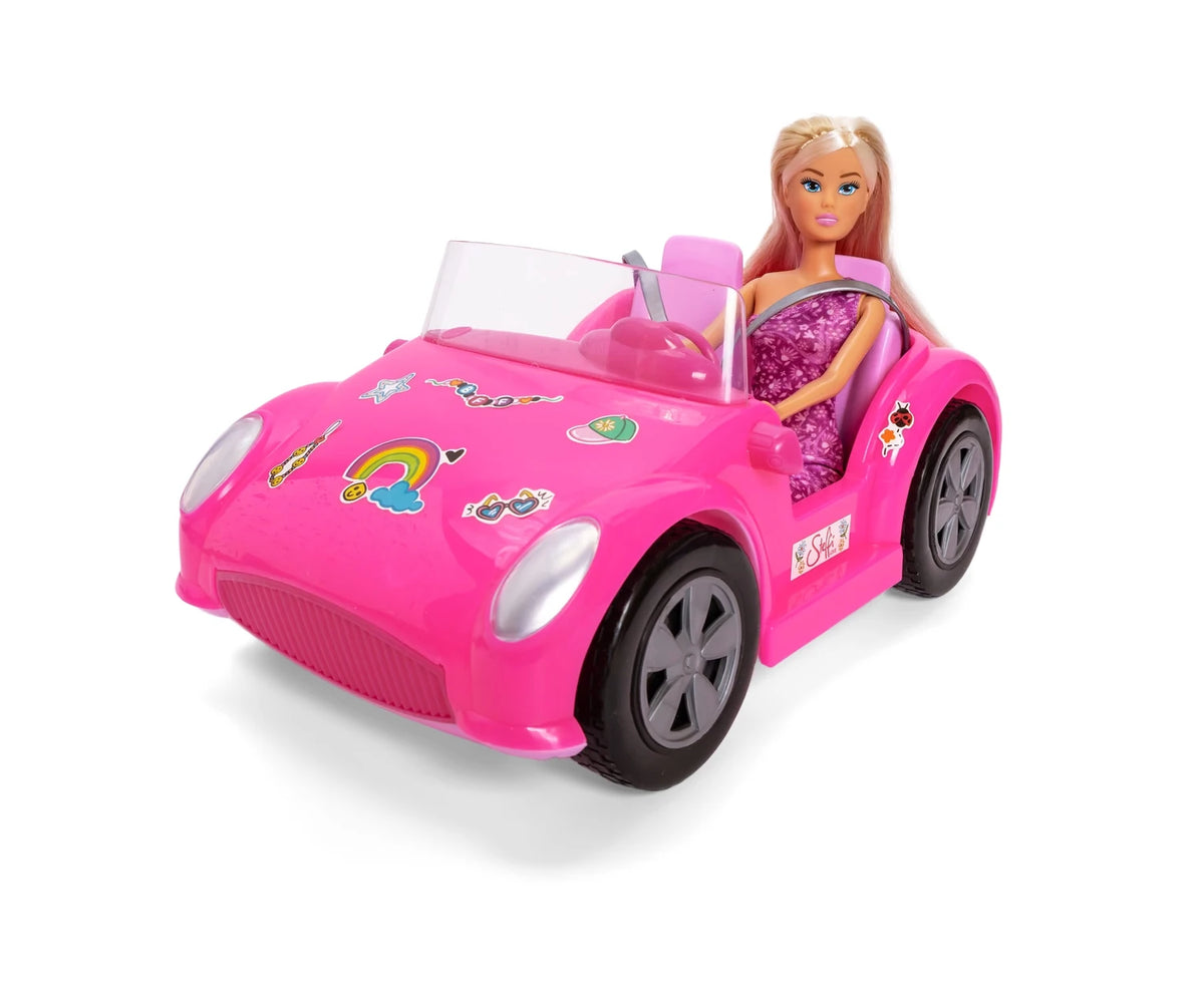 Steffi Love doll wearing a purple floral dress seated in a bright pink convertible with grey wheels, transparent windscreen and colourful stickers on the bonnet.