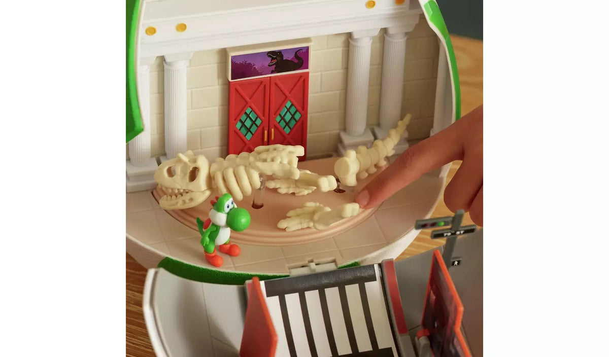 Museum interior of the Yoshi Egg Playset showing Yoshi beside a cream dinosaur skeleton lying across the display floor, with a hand touching one of the bone pieces.