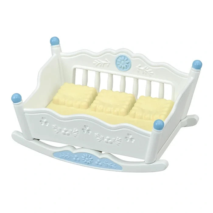 Empty white Sylvanian Families rocking cradle with blue finials, floral decorations and a yellow mattress with three raised sleeping sections.