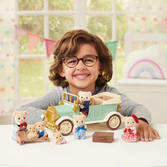 Child sitting behind the Sylvanian Families Classic Family Car with animal figures arranged around the vehicle and picnic accessories.