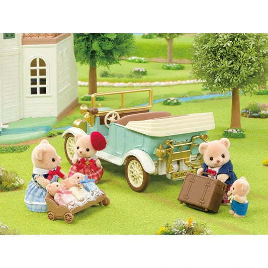 Sylvanian Families animal figures gathered around a pram and picnic accessories beside the Classic Family Car near a house and garden.