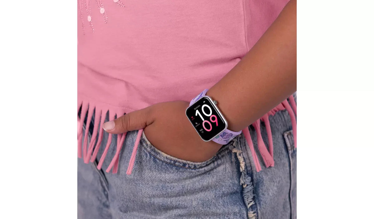 Tikkers unicorn smartwatch worn on a wrist with a black and pink digital watch face, beside a pink fringed top and blue jeans.