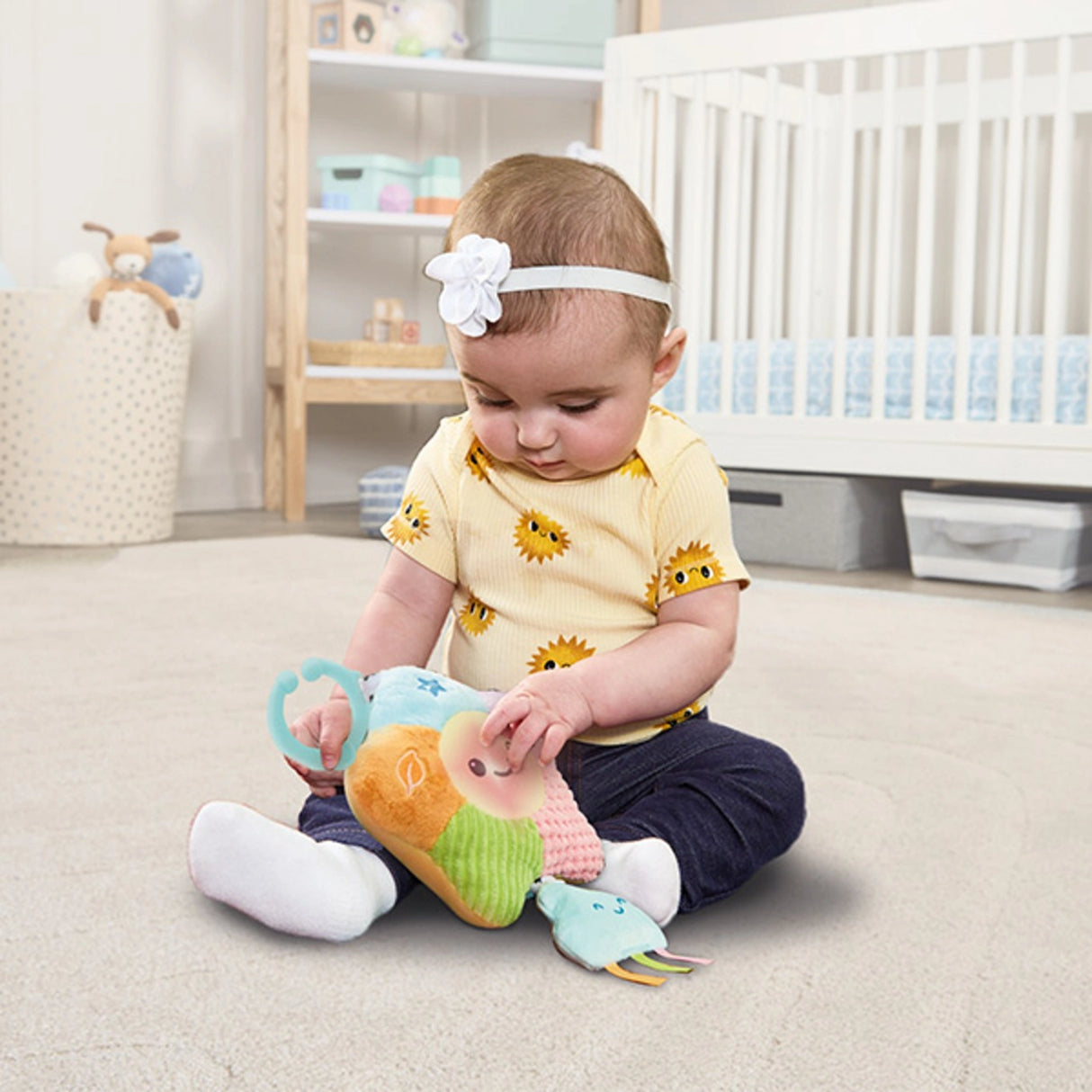 Baby sitting on nursery floor holding VTech Baby Soothing Sounds Star toy with C ring clip and soft cloud attachment