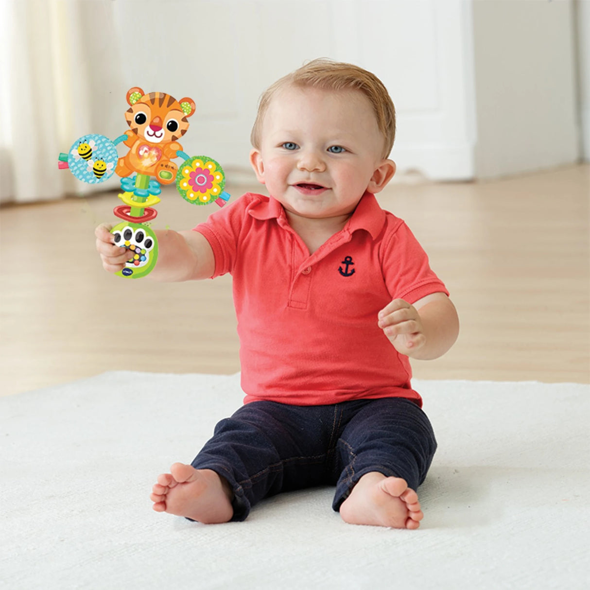 Baby seated on light coloured mat holding VTech Rattle & Roar Tiger rattle upright in right hand