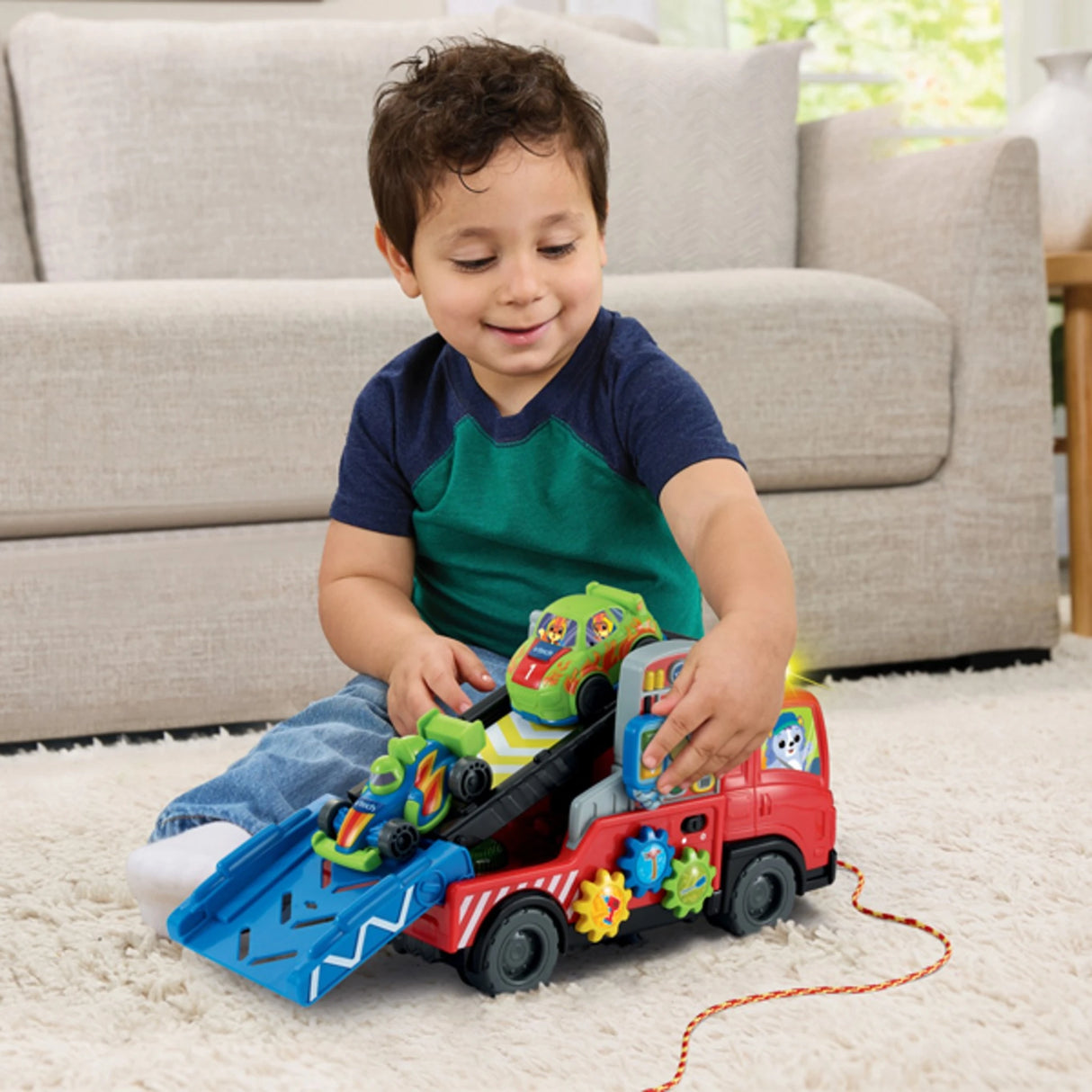 Child sitting on carpet playing with VTech Road Rescue Car Carrier with ramp lowered and green and blue sports cars loaded