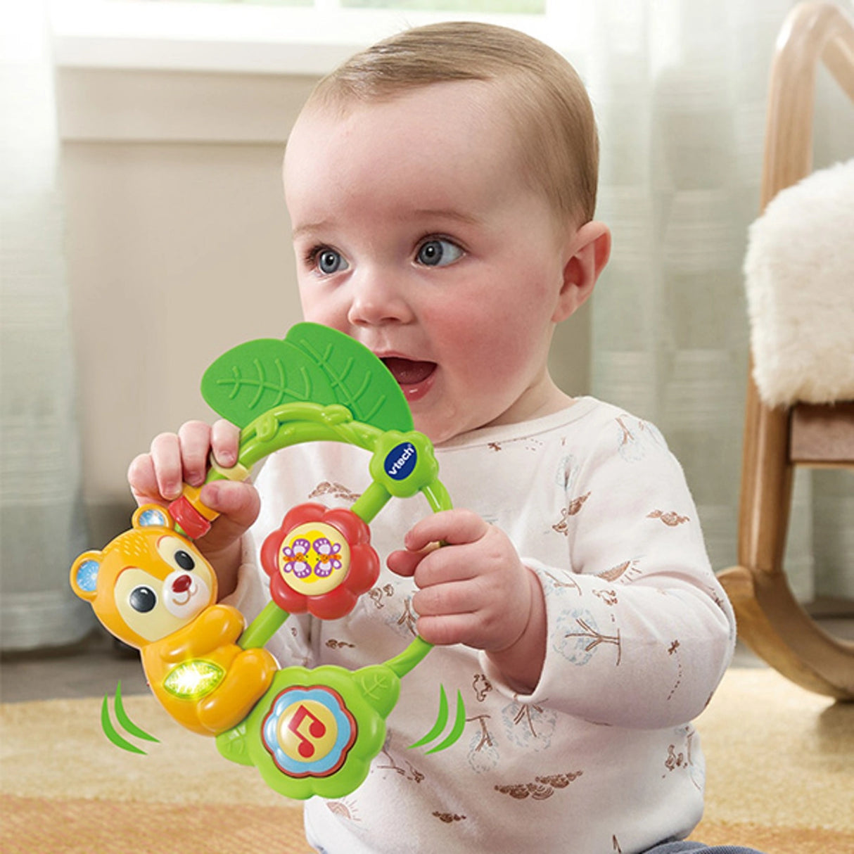 Baby holding VTech Shaking Sounds Bear Rattle with green leaf teether, red flower spinner, music note button and motion lines around the toy