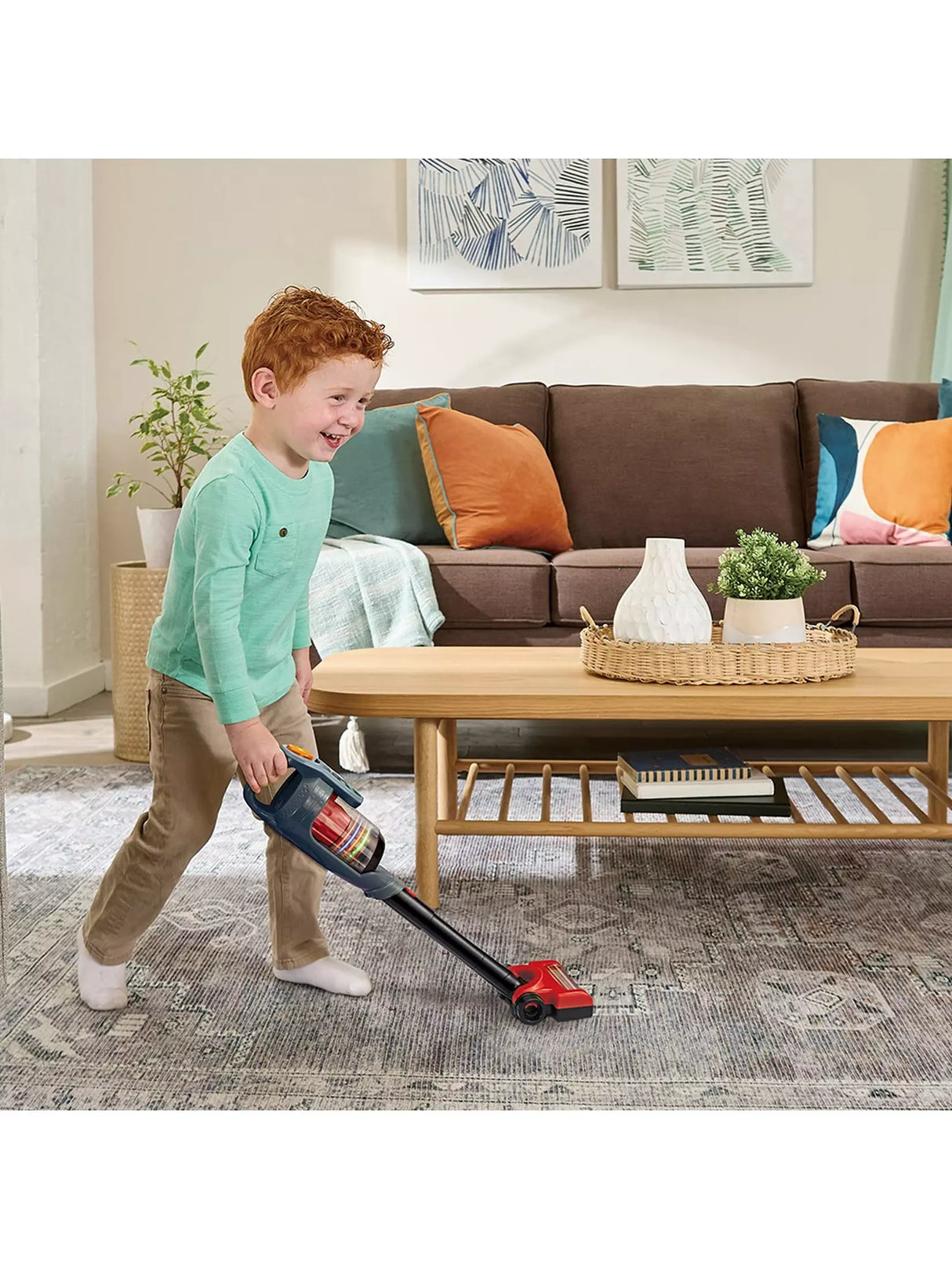 VTech Tidy Up Vacuum with a child in a green top holding the stick vacuum over a patterned rug