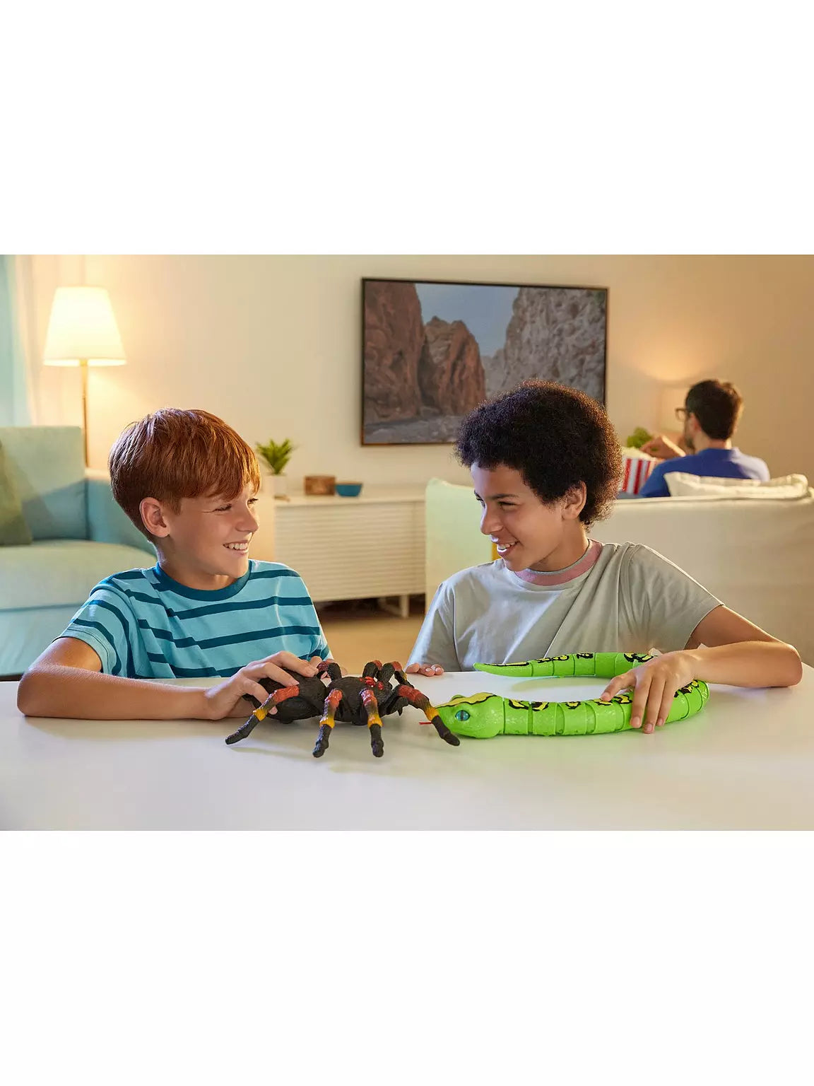 Two children playing with the Zuru Robo Alive Giant Tarantula on a table beside a green snake toy
