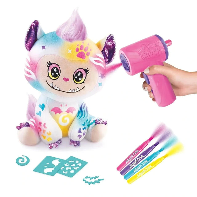 Airbrush Plush Cutie Monster decorated with pink, yellow, blue and purple patterns while a hand sprays pink colour onto its ear using the airbrush, with four markers and turquoise stencils displayed underneath.