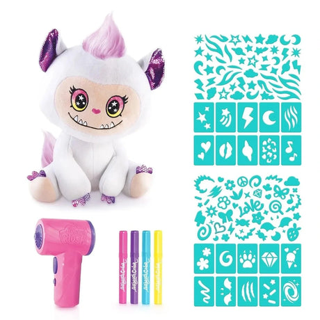 White Airbrush Plush Cutie Monster with pink hair and purple ears, displayed beside a pink airbrush tool, four pink, purple, blue and yellow markers, and turquoise stencil sheets featuring stars, hearts, lightning bolts and other patterns.