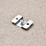 Close-up of the silver metal dartboard mounting bracket with two fixing holes and a central screw on a wooden surface.