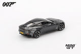James Bond Aston Martin DBS grey RHD prototype viewed from the rear left showing the rear light strip, boot spoiler, black roof and yellow number plate