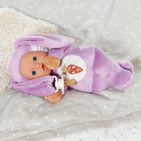 BABY born Funny Bunny lying on bed with dummy secured to the ear clip