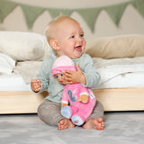 Baby Born For Babies Sleepy Pink doll cuddled by smiling baby sitting beside a bed